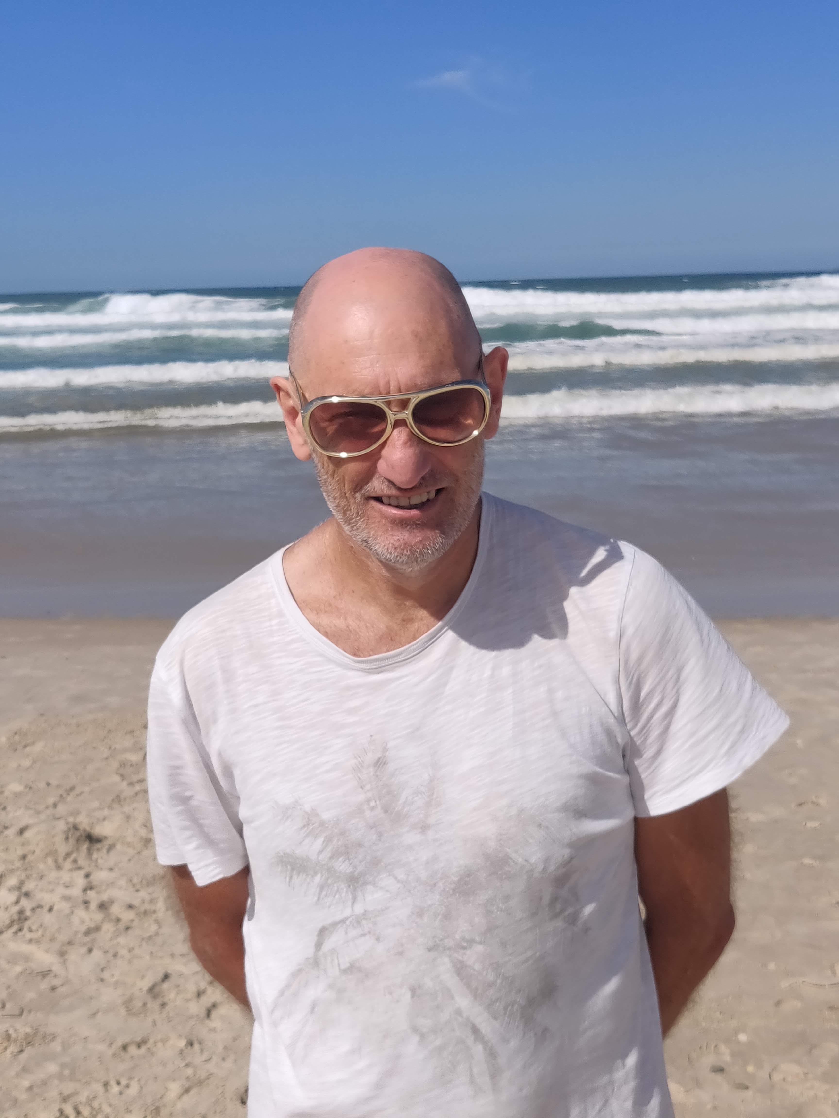 image of a man standing on the beach, smiling facing the camera