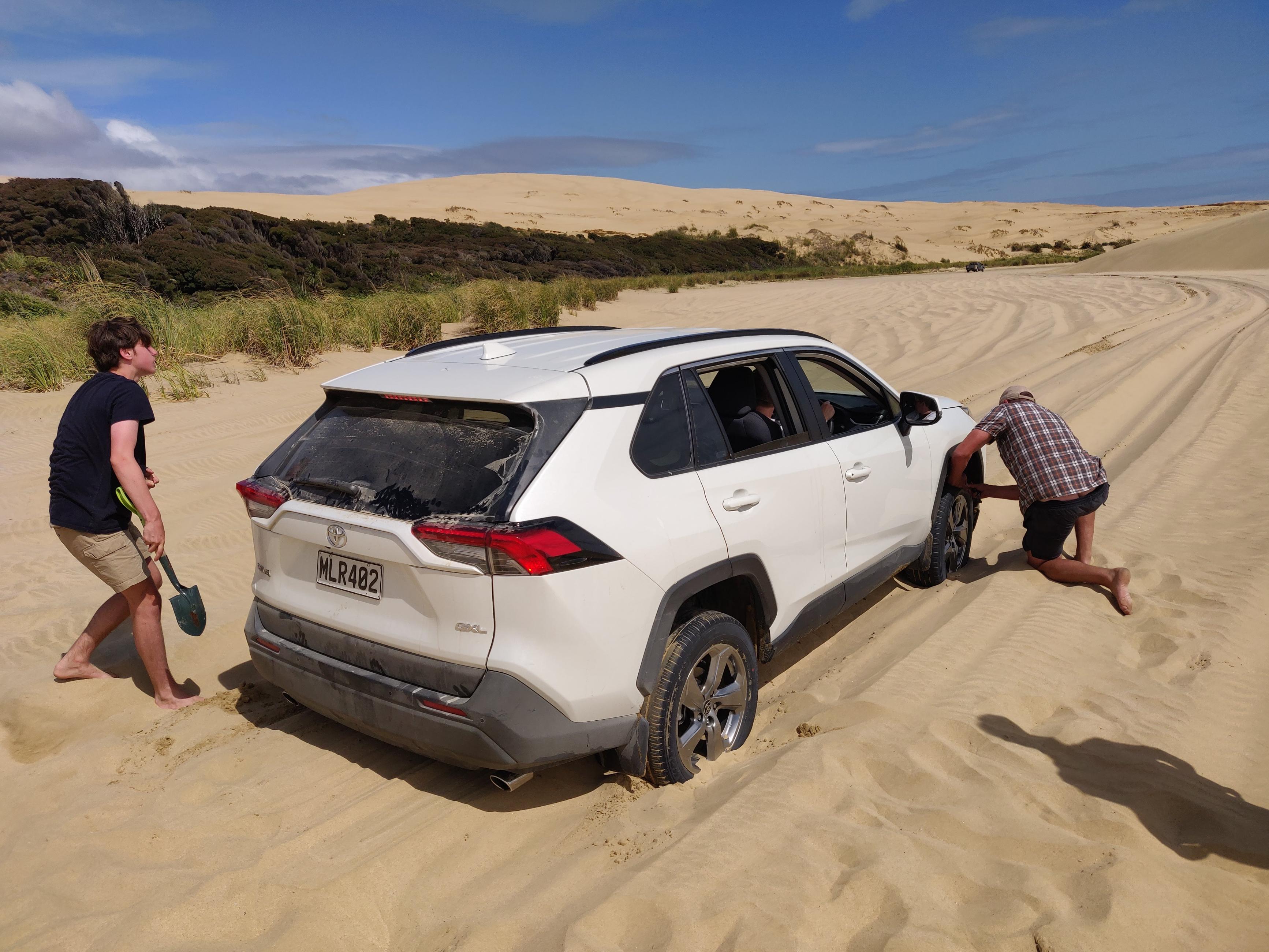 image of a father and his son struggling to free a trapped car which has sunken into the soft sand