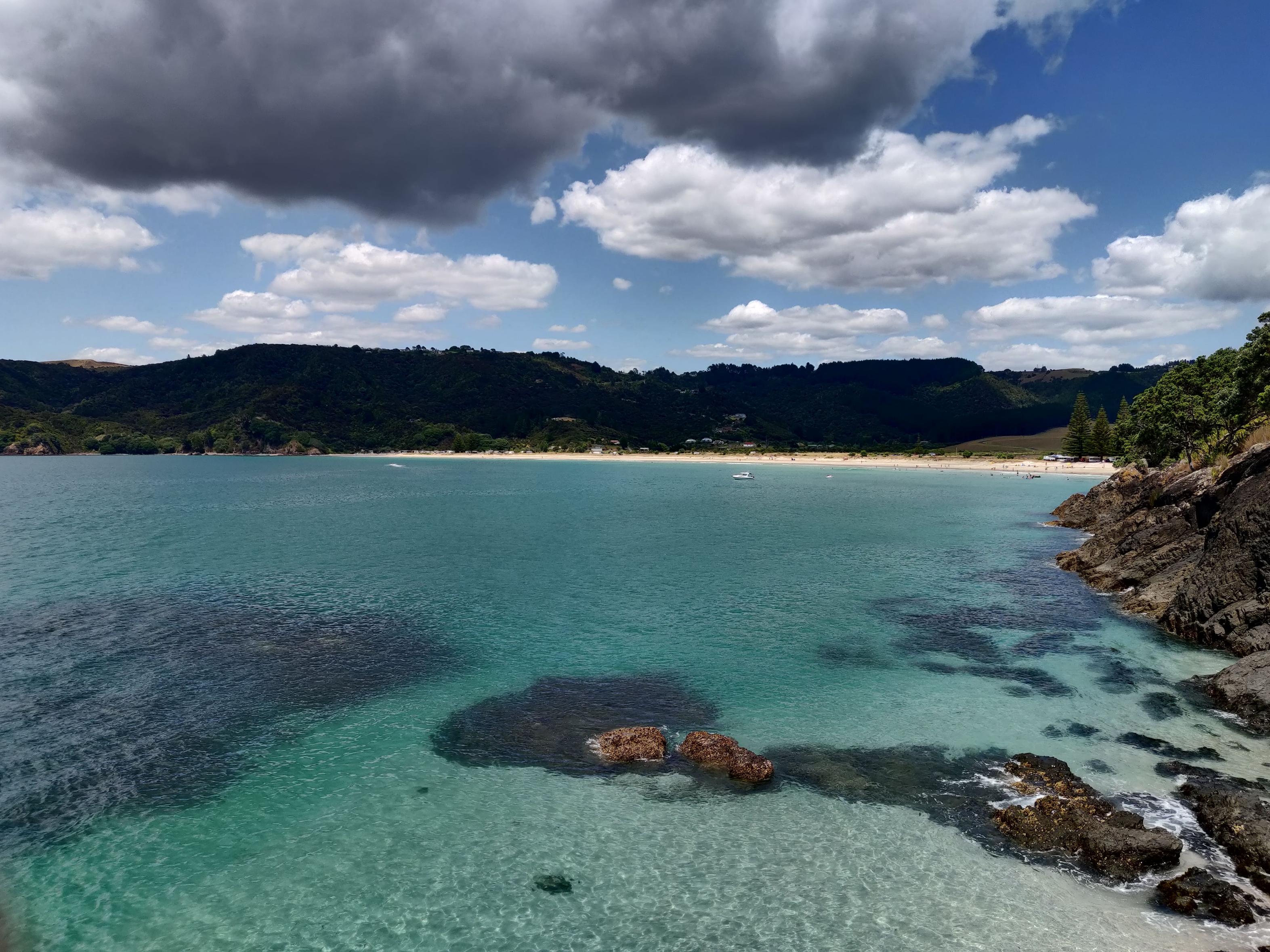 image of the ocean meeting the beach, with a distant campground in the background
